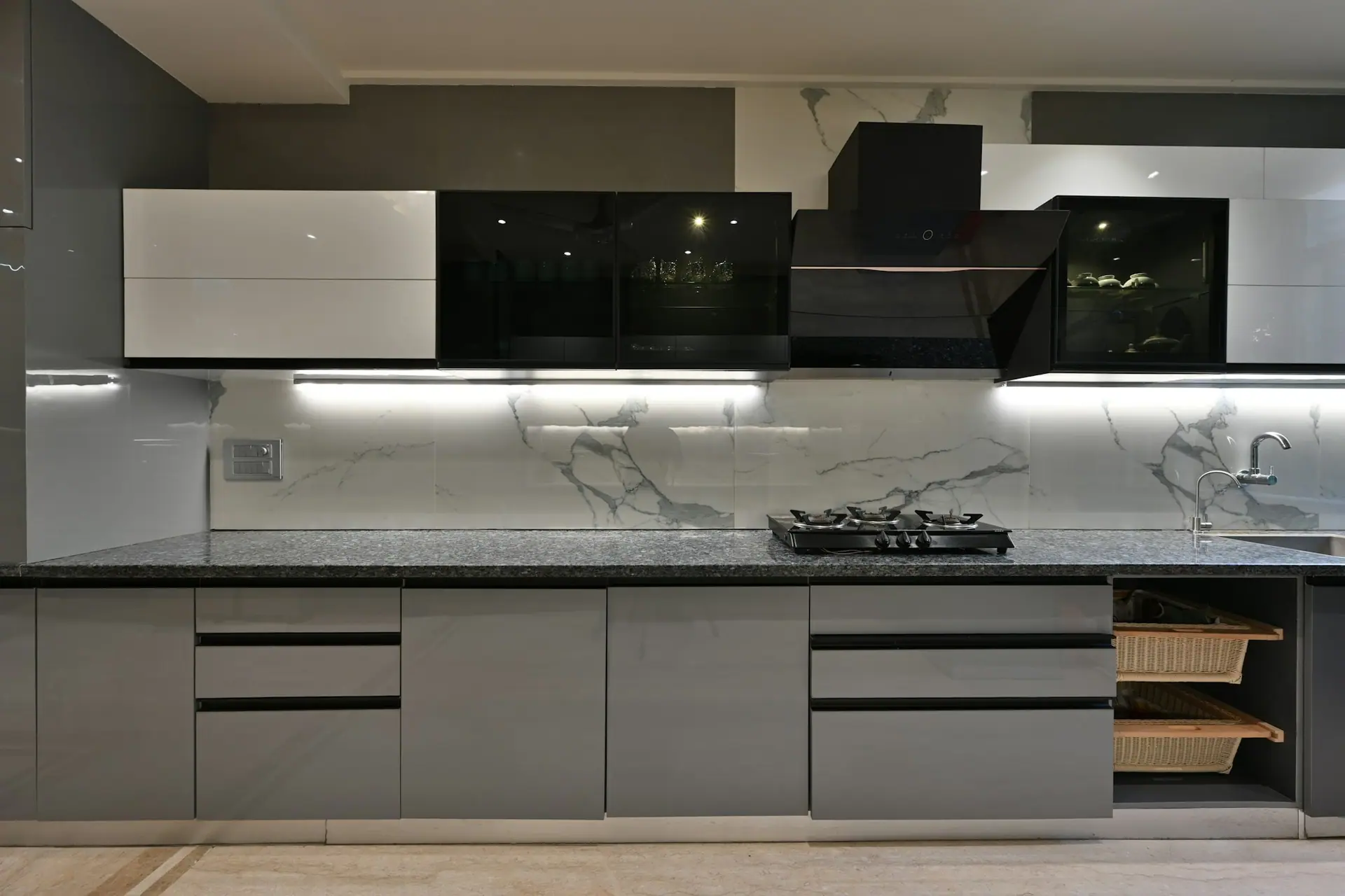 Modern kitchen with grey gloss base cabinets, black glass wall units, a chimney over a glass gas hob and a granite counter