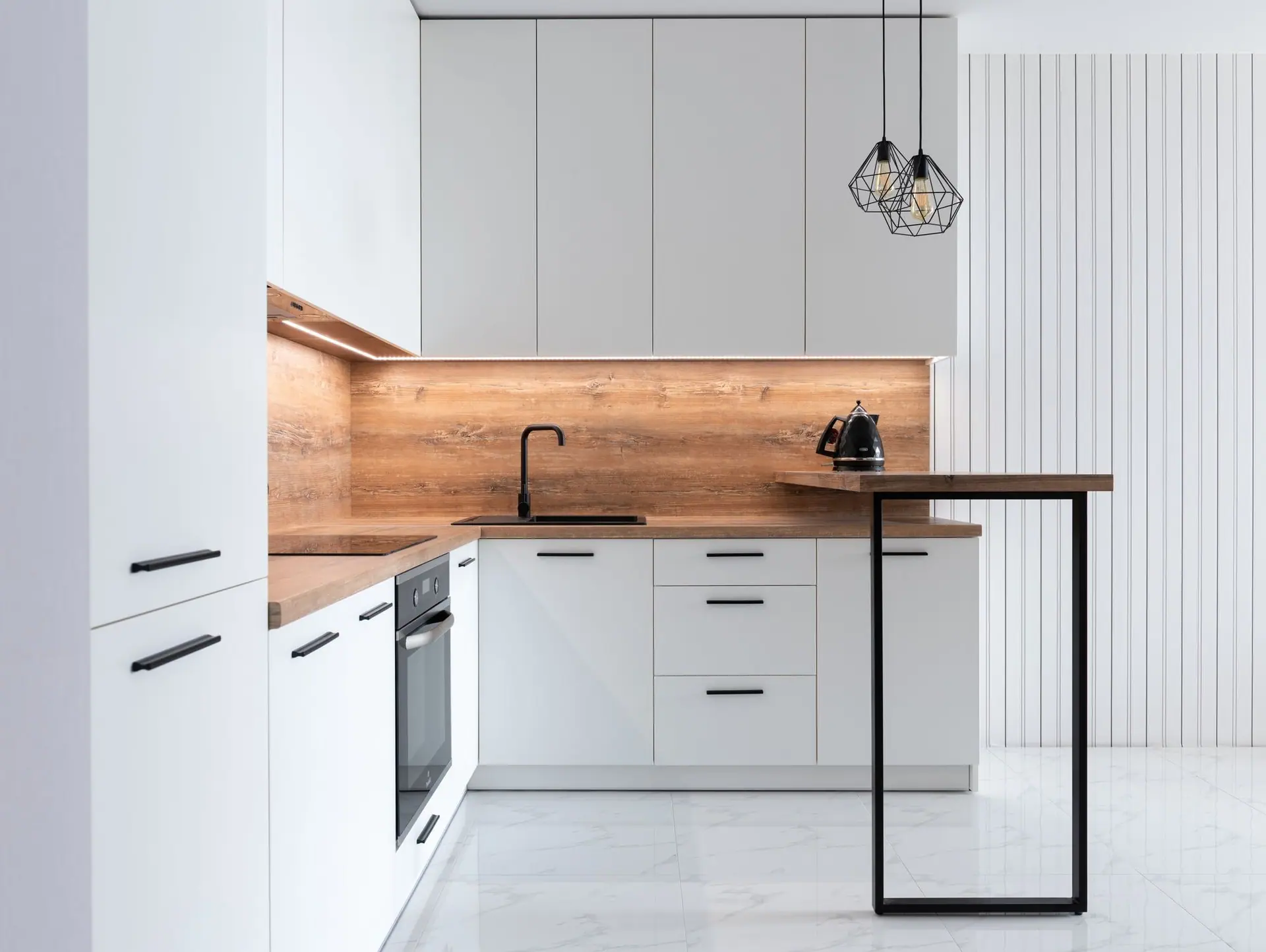 White L-shaped kitchen with an oak worktop, lit backsplash and tall storage units