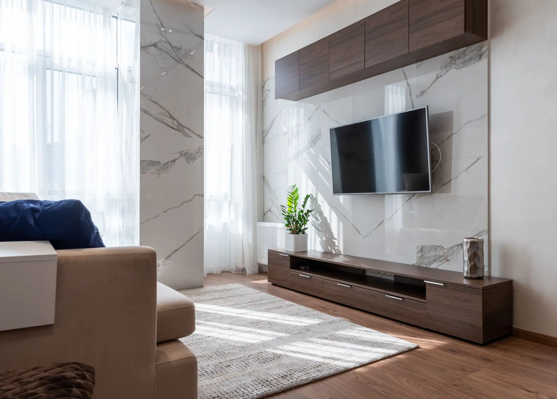 Walnut floating TV unit and wall cabinets on a white marble feature wall in a sunlit living room